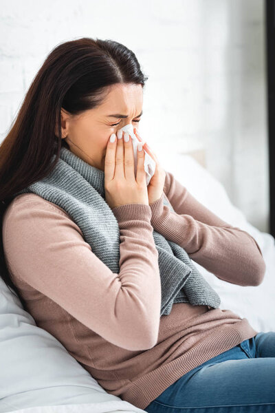 beautiful ill woman in scarf with runny nose holding napkin at home