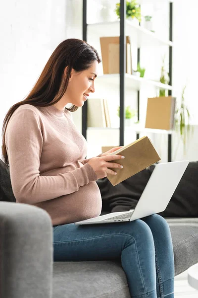 Těhotná Žena Drží Knihu Zatímco Line Konzultace Lékařem Notebooku Doma — Stock fotografie