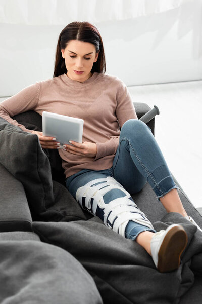 серьезная женщина со сломанной ногой, имеющая онлайн консультацию с врачом на цифровом планшете дома
