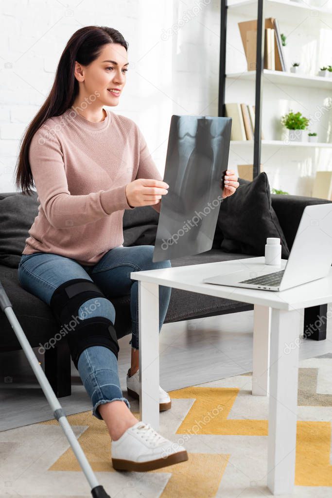 Woman showing x-ray of leg on online consultation with doctor on laptop at home