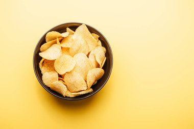 top view of delicious crispy potato chips in bowl on yellow background clipart