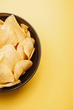 top view of delicious crispy potato chips in bowl on yellow background clipart