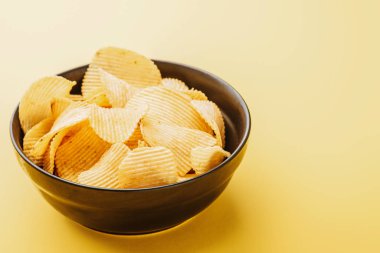 delicious crispy potato chips in bowl on yellow background clipart