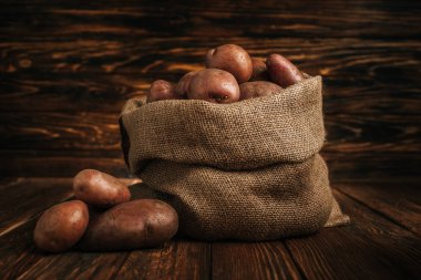 ripe potatoes in rustic sack on wooden background clipart