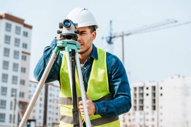 Surveyor looking throughout digital level on construction site  clipart