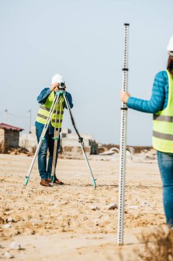 Selective focus of surveyors working with ruler and digital level on construction site clipart