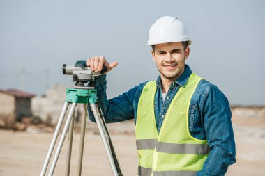 Smiling surveyor with digital level looking at camera clipart