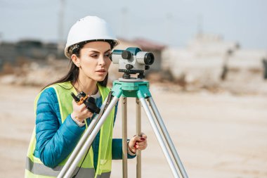 Female surveyor with radio set looking through digital level  clipart