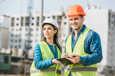 Female surveyor talking to smiling colleague with clipboard clipart