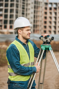 Surveyor holding digital level with construction site at background clipart