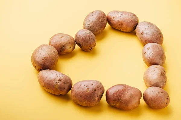 Patatas Frescas Enteras Crudas Dispuestas Corazón Sobre Fondo Amarillo — Foto de Stock