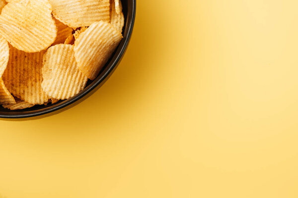 top view of delicious crispy potato chips in bowl on yellow background