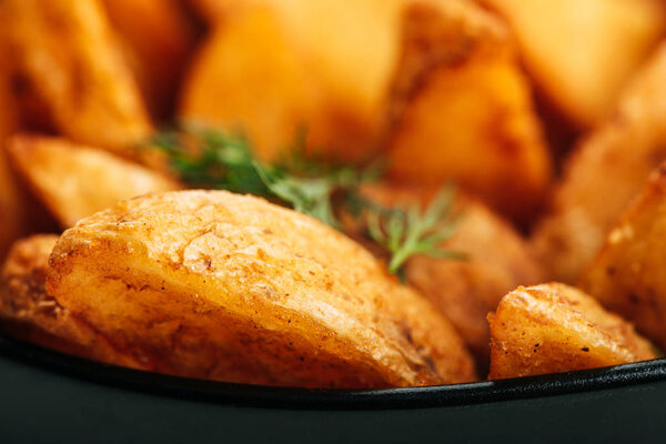 close up view of delicious golden potato wedges with dill in bowl