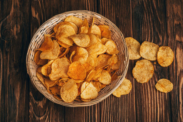 top view of delicious crispy potato chips in wicker basket on wooden table