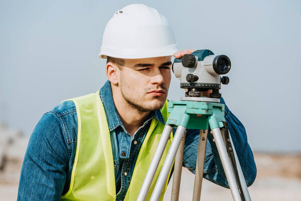 Surveyor in hardhat and high visibility jacket using digital level 