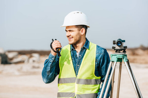 Smiling surveyor with digital level talking on radio set 