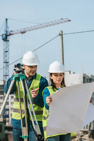 Surveyors with digital level looking at blueprint on construction site