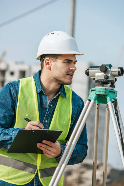 Surveyor with clipboard looking throughout digital level 