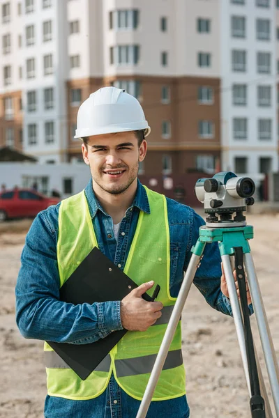 Surveyor Holding Clipboard Digital Level Smiling Camera Construction Site — Stock Photo, Image