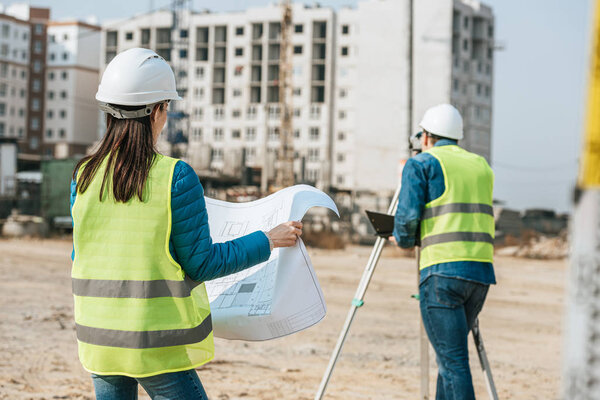 Surveyors with blueprint and digital level working on construction site