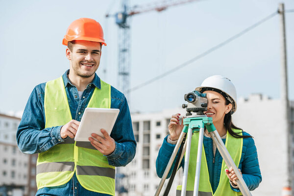 Smiling surveyors with digital tablet and measuring level on construction site
