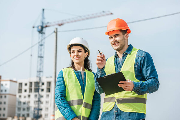 Smiling surveyor with clipboard pointing away to colleague on construction site