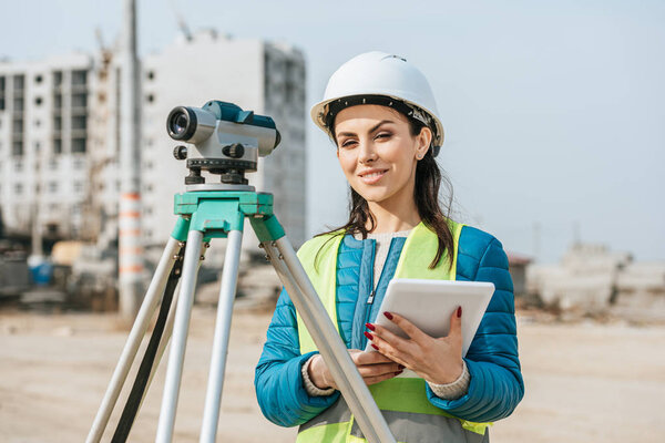 Surveyor with digital tablet and measuring level smiling at camera