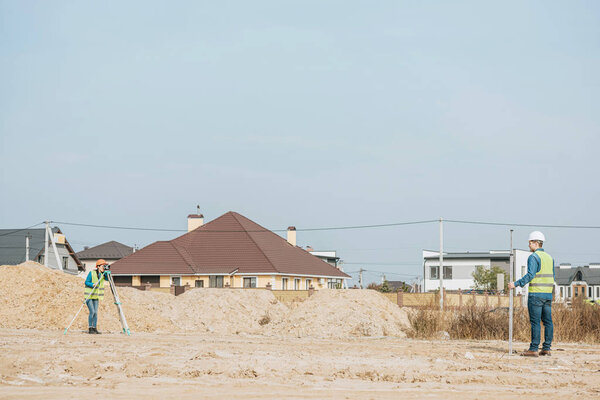 Surveyors with digital level ruler on working on dirt road with sand mounds