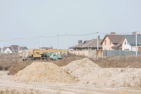 Sand molds on dirt road with building crane and houses at background