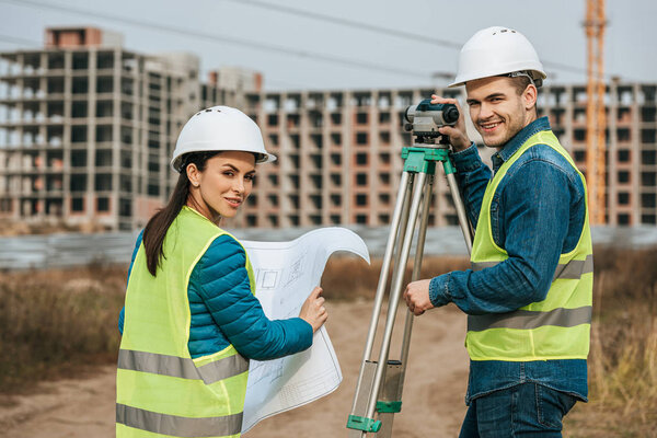 Smiling surveyors with blueprint and digital level 