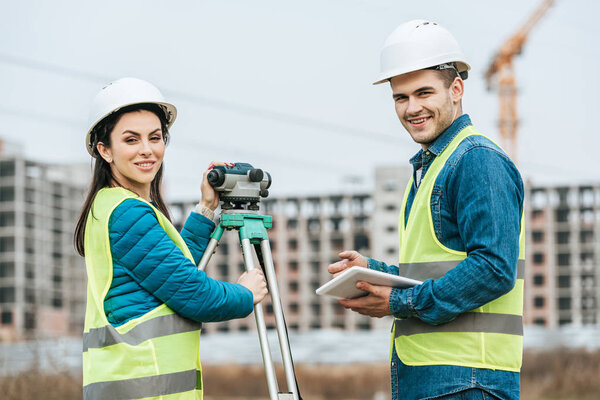 Smiling surveyors with digital level and tablet looking at camera