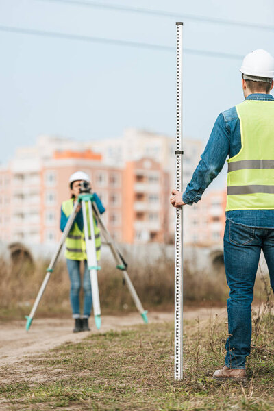 Selective focus of surveyors measuring land with digital level and ruler
