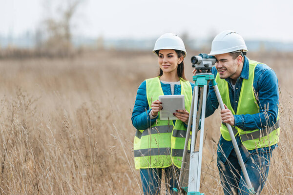 Smiling surveyors with digital level and tablet in field