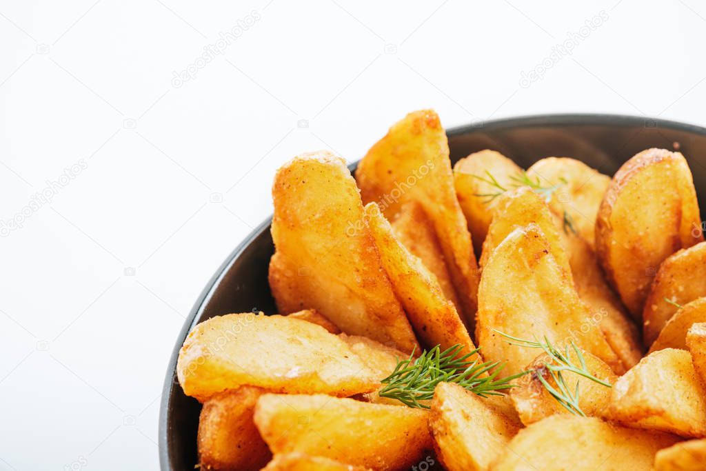 close up view of delicious golden potato wedges with dill in bowl isolated on white