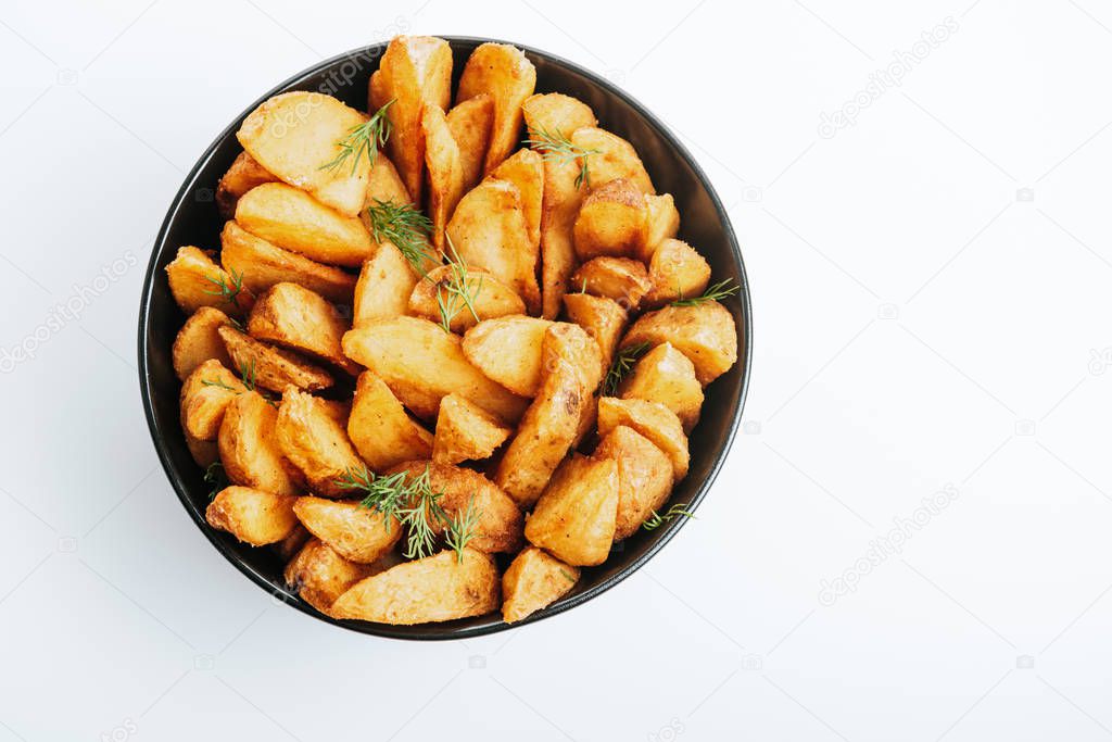 top view of delicious golden potato wedges with dill in bowl isolated on white