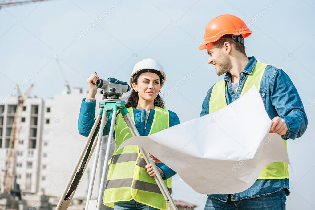 Smiling Surveyors with blueprint and digital level