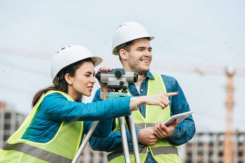Surveyor looking through digital level and pointing away to colleague with tablet