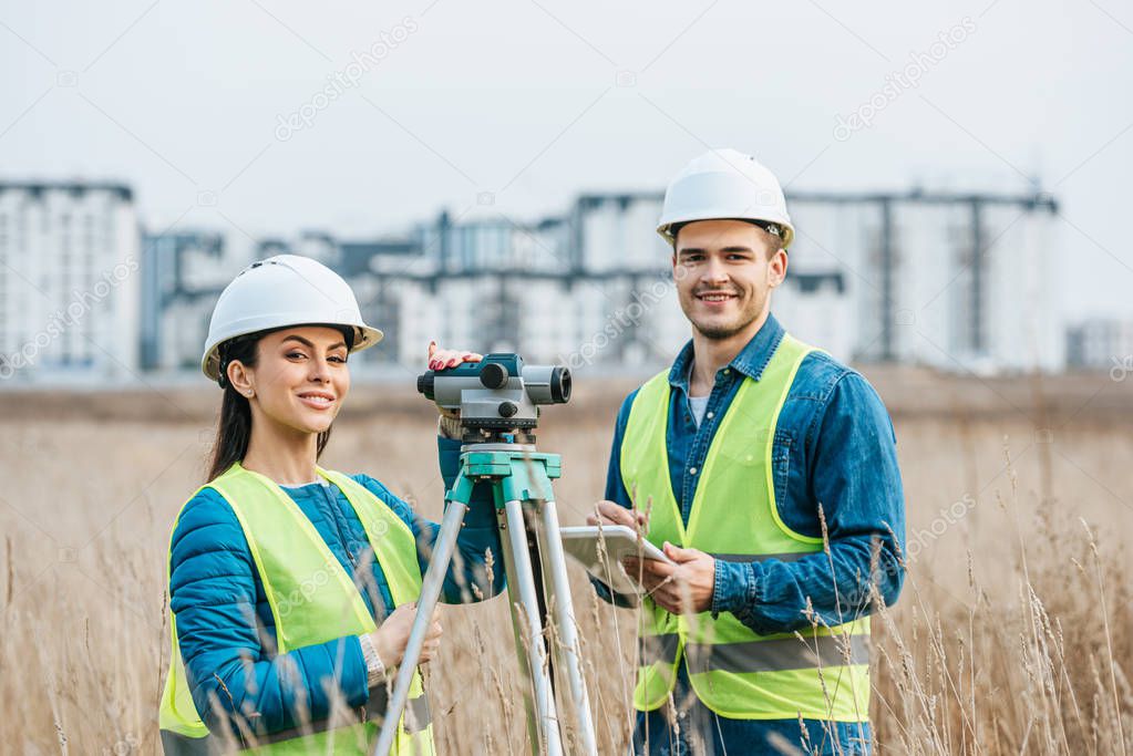 Smiling surveyors with digital level and tablet looking at camera in field