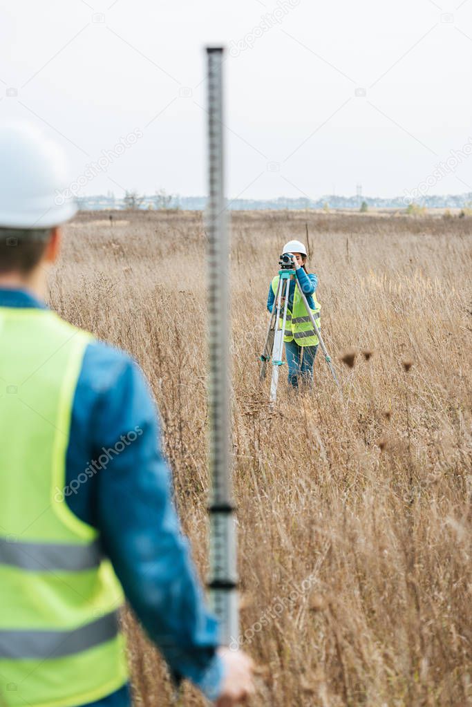 Selective focus of surveyors with digital level and ruler working in field