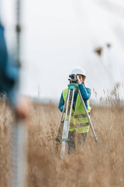 Selective focus of surveyors measuring land with digital level and ruler in field clipart