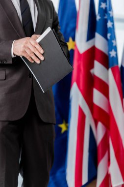 Takım elbiseli diplomatın bayrakların yanında klasör tutması. 