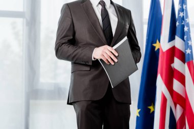cropped view of ambassador in suit holding folder near flags  clipart