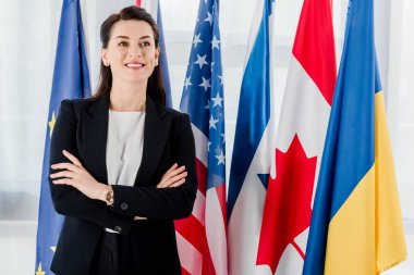 Bayrakların yanında kollarını kavuşturmuş mutlu bir diplomat. 