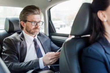 selective focus of handsome diplomat in glasses sitting with woman in car clipart