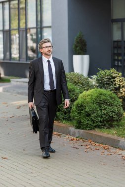 Gözlüklü yakışıklı diplomat evrak çantası tutuyor ve binanın yanında duruyor. 