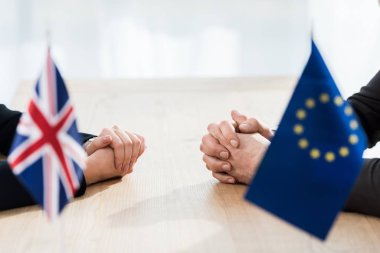 Avrupa Birliği ve Birleşik Krallık bayrakları yakınında elleri sımsıkı bağlı oturan büyükelçi görüşü 