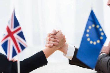 Avrupa Birliği ve Birleşik Krallık bayrakları yakınında el ele tutuşan büyükelçiler 