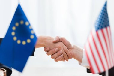 selective focus of diplomats shaking hands near flags of usa and european union clipart
