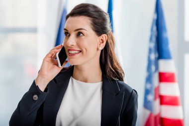Amerikan bayrağı yakınında akıllı telefondan konuşan mutlu bir diplomat. 