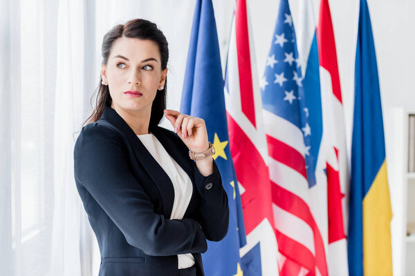 attractive diplomat looking away while standing near flags 